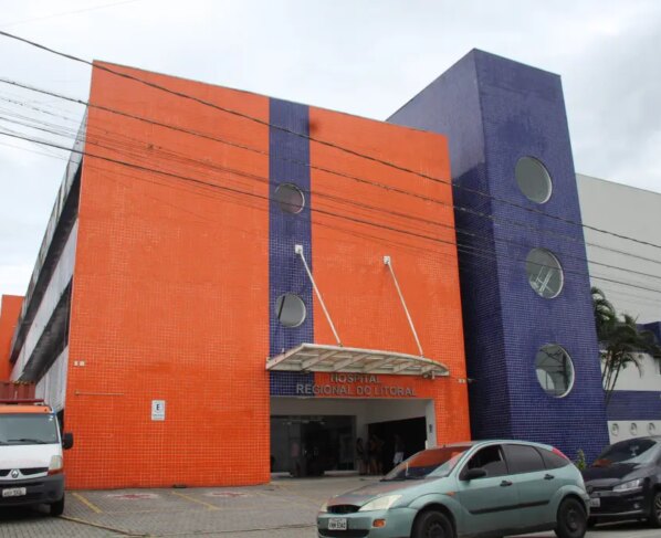Imagem do Hospital Regional do Litoral, com fachada colorida em tons de laranja e roxo, destaque para a entrada e veículos estacionados. Governo investe R$ 5,1 milhões para reforçar atendimento no Hospital Regional do Litoral