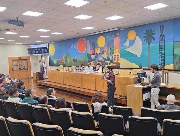 Público no Auditório Prestes Maia acompanha fala de participante em reunião sobre direito dos migrantes, promovida pela vereadora Luna Zarattini.