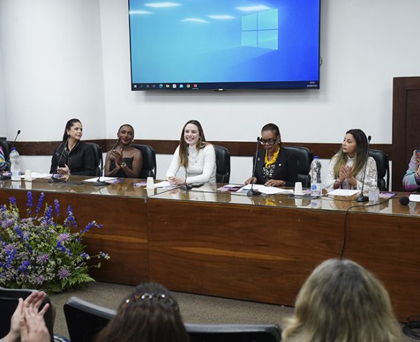 Mesa de solenidade do Agosto Lilás na Câmara Municipal de São Paulo, com a vereadora Zoe Martínez e mulheres palestrantes em destaque.