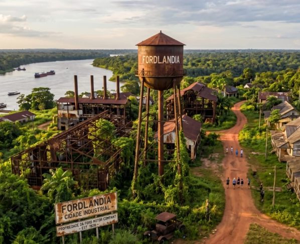 Imaginei o ângulo perfeito: uma foto de drone que captura a gigantesca caixa d'água de metal, com a marca "FORDLANDIA" ainda visível, erguendo-se sobre a selva amazônica tropical