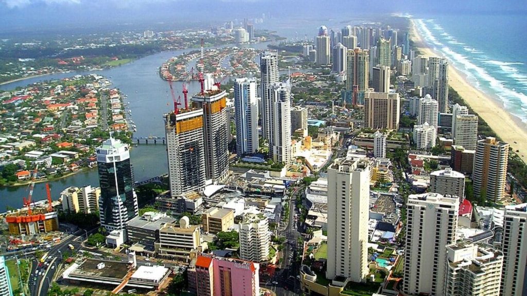 Vista aérea de Gold Coast, na Austrália, com prédios altos próximos à praia, canal com casas ao redor e faixa extensa de areia ao lado do mar