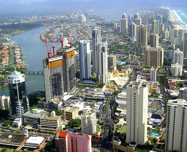 Vista aérea de Gold Coast, na Austrália, com prédios altos próximos à praia, canal com casas ao redor e faixa extensa de areia ao lado do mar